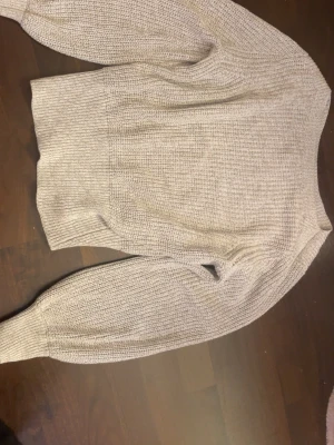 Beige stickad tröja från H&M - Mysig beige stickad tröja från H&M med rund halsringning och bred ribbad mudd vid ärmslut och nederkant. Perfekt för lager på lager och enkel att matcha till olika outfits.