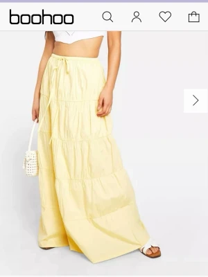 Gul långkjol med snörning från Boohoo - Ljusgul långkjol från Boohoo med avslappnad passform och snörning i midjan. Kjolen har flera volanger och är tillverkad i ett lätt bomullstyg, perfekt för varma dagar. Enkel och trendig design som passar till många olika stilar.