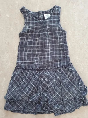 Klänning - Snygg grå ärmlös klänning från H&M i rutigt mönster. Klänningen har en avslappnad passform med volang nedtill och är tillverkad i mjuk bomull. Perfekt för dig som gillar en enkel men trendig stil.