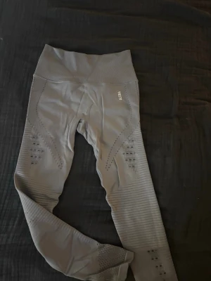 Grå seamless leggings från ALERA - Snygga grå seamless leggings från ALERA med hög midja och ribbade detaljer längs sidorna. Materialet är stretchigt och har ventilerande meshpaneler för extra komfort. Aldrig använda