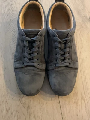 Mörkgrå Louboutin - Snygga mörkgrå sneakers med rund tå och snörning. Skorna är tillverkade i mocka och har en låg profil med platt sula. Insidan är ljusbeige vilket ger en schysst kontrast till utsidan. Perfekta för dig som gillar stilrena och klassiska sneakers. Skicka vid frågor