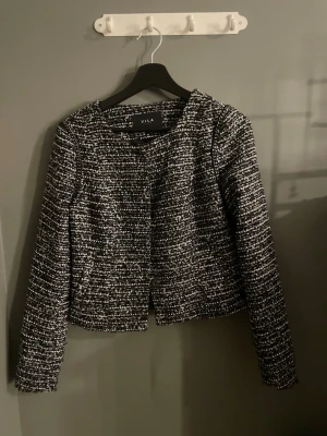 Svartvit kavaj från Vila - Stilren svartvit kavaj från Vila med rutigt mönster och rund halsringning. Kavajen är långärmad och har en croppad passform som ger en modern look. Perfekt att matcha med både jeans och kjol för en trendig outfit.