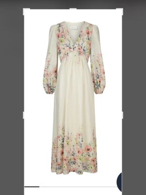 Blommig maxiklänning från Neo Noir - Romantisk långklänning i ljusbeige med blommigt mönster i rosa, orange och blå toner. Klänningen har långa puffärmar, v-ringning och markerad midja. Perfekt för sommarens alla tillfällen. Storlek 40 .Använd vid ett tillfälle.