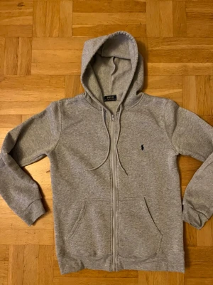 Grå zip hoodie från Polo Ralph Lauren - Grå polo zip använd 1 gång. Säljer då den inte passar. Priset kan diskuteras. Skriv för fler frågor !