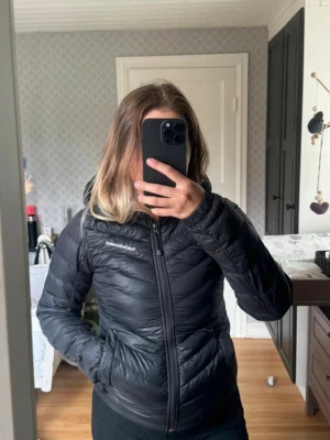 Svart dunjacka från Peak Performance - Snygg svart dunjacka från Peak Performance med huva och dragkedja framtill. Jackan är har två fickor med dragkedja. Perfekt för kalla dagar och enkel att matcha med allt.