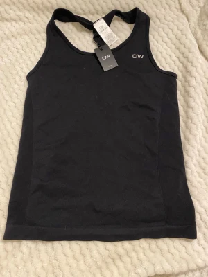 Svart träningstopp från ICANIWILL - Snygg svart träningstopp från ICANIWILL med brottarrygg och diskret logga framtill. Tillverkad i ett stretchigt funktionsmaterial som andas, perfekt för gymmet eller löprundan. Enkel och stilren design som ger bra rörelsefrihet.