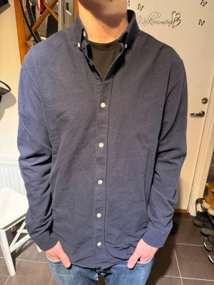 Jack and Jones skjorta  - Stilren mörkblå skjorta från Jack and Jones med klassisk button-down krage och vita knappar. Skjortan är långärmad och har en normal passform. Perfekt för dig som gillar enkel och tidlös stil. Andvänd max 5 gånger