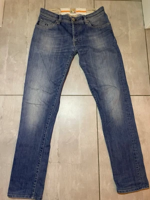 Blå jeans från Tramarossa  - Säljer ett par Tramarossa jeans med raka ben och normal passform. Jeansen har fem fickor, snygga slitningar och en ikonisk Tramarossa-lapp bak. Perfekta till vardags för en avslappnad look. Nypris:2200kr. Liten defekt på baklappen som lätt och billigt kan fixas hos en skräddare. Vid funderingar fråga gärna