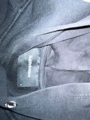 Svart hoodie från Peak Performance - Svart hoodie från Peak Performance med vit logga tryckt på bröstet. Klassisk modell med huva och dragsko samt magficka framtill. Tillverkad i mjukt material som känns skönt mot huden. Storleken är L men den passar nästan mig! 