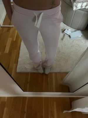 Ljusrosa mjukisbyxor med snörning - Säljer ett par ljusrosa mjukisbyxor med vit snörning i midjan. Byxorna har en relaxed passform och är perfekta för chill dagar. Mjukt material som känns skönt mot huden och bred mudd i midjan för extra komfort.