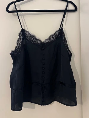 Spetslinne  - Snygg mörkblå linnetopp med tunna axelband och dekorativa knappar framtill. Toppen har v-ringning och spetsdetaljer längs urringningen som ger en elegant touch. 