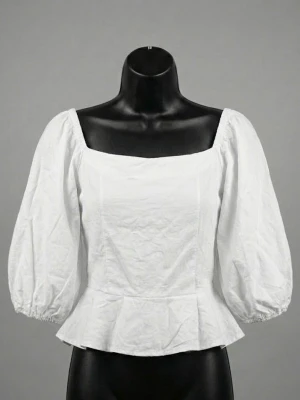 Vit blus med puffärm och dragkedja - Säljer en vit blus med fyrkantig ringning, puffiga trekvartsärmar och volangkant nedtill. Toppen har smockad rygg och dragkedja bak för enkel påklädning. Tillverkad i ett lätt bomullstyg som känns luftigt och fräscht.
