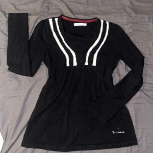 Svart långärmad - Svart långärmad blus från Bondelid med vita virkade detaljer längs v-ringningen och knappar framtill. Fint skick och aldrig använd. Blusen har ett knytband i midjan och broderad logga nertill. Går att knyta framtill eller baktill, det kan du välja utifrån preferens 🤗