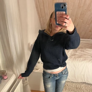 Mörkblå stickad hoodie med huva - Mysig mörkblå stickad hoodie från Gina Tricot med huva och snörning. Tröjan har lång ärm, ribbad nederkant och en loose passform. Perfekt för kyliga dagar när du vill vara både bekväm och snygg.