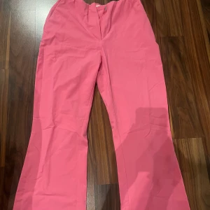 Rosa bootcut byxor med stretch - Säljer ett par snygga rosa bootcut byxor med lätt utsvängda ben och elastisk midja. Byxorna har en enkel design utan synliga detaljer framtill två fickor. Perfekta för dig som vill sticka ut med färg.