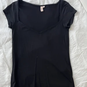 Svart kortärmad topp med spetsdetalj - Snygg svart figursydd topp från Nelly med korta ärmar och en v-ringad halslinje med spets. Skitsnygg men tyvärr för liten på mig, har aldrig använts. Storlek S