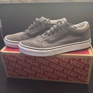 Grå Vans Old Skool sneakers  - Säljer ett par klassiska Vans Old Skool sneakers i grå mocka med svarta detaljer och vit sula. Säljs då dem blivit för små. Hör gärna av dig vid frågor eller funderingar. Pris kan diskuteras vid snabb affär!