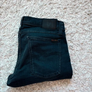 Svarta jeans från Nudie Jeans - Säljer ett par svarta jeans från Nudie Jeans Co i storlek W32 L34. Jeansen sitter slim fit, svarta sömmar och Nudie-logga på bakfickan. Perfekt för dig som vill vara oldmoney/Grish, vid ytterligare funderingar så är det bara att höra av sig.🌟🤩