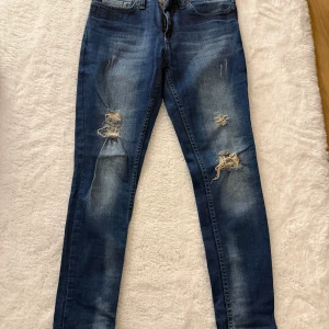 Blå slitna jeans från J Pull, W26 - Snygga blå jeans från J Pull i modellen Boyfriend. Jeansen har slitna detaljer och hål på båda benen för en trendig look. De är tillverkade i klassiskt denimtyg och har en relaxed passform med raka ben. Perfekta för dig som gillar en avslappnad stil.