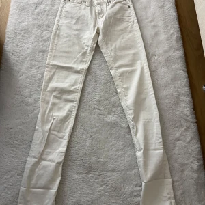 Vita Replay jeans, midja 25 längd 34 - Snygga vita jeans från Replay med klassisk femficksdesign och raka ben. Byxorna har normal passform och är tillverkade i ett mjukt bomullstyg som sitter skönt hela dagen. Perfekta för dig som gillar stilrena och ljusa jeans.
