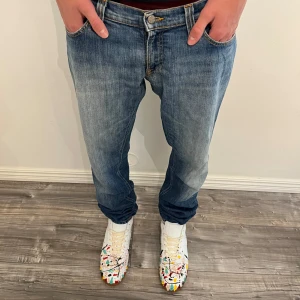 Blå Nudie Jeans  - Vintage Nudie jeans. Säljer ett par klassiska blå jeans från Nudie Jeans med snyggt slitna detaljer och kontrastsömmar. Modellen har raka ben och femficksdesign, samt Nudie-logga på bakfickan. Perfekta för dig som gillar en tidlös och avslappnad look.