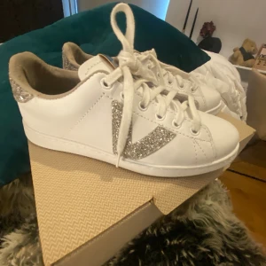 Vita sneakers med glitterdetaljer - Snygga vita sneakers med glittriga silverdetaljer på hälen och ett stort V i glitter på sidan. Använd 1 gång storlek 37 
