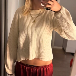 Beige stickad tröja från Selected Femme - Supermysig beige stickad tröja från Selected Femme med ribbad struktur och lite croppad passform. Tröjan har långa ärmar och en rund halsringning. Perfekt för lager-på-lager och chill dagar.