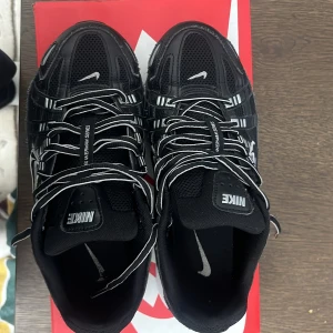 Nike P-6000 svarta sneakers - Nästan helt nya Nike P-6000 sneakers i svart med vita detaljer och reflekterande ränder. Ovandel i mesh och syntet, med tydlig snörning och robust, vit och svart sula. Swoosh-logga på sidan och Nike-märke på plösen. Perfekta för dig som gillar sportig och modern stil.