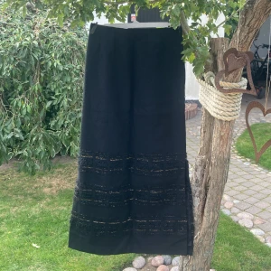 Svart långkjol från Arola i ull XS - Säljer en svart långkjol från Arola, tillverkad i Finland. Kjolen är i ull och har snygga broderade detaljer med inslag av guldtråd nertill. Rak modell med slits i sidan, perfekt för dig som gillar unika vintageplagg.