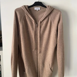 Davida Cashmere Zip Hoodie - Mysig beige zip hoodie från Davida Cashmere i lyxig och skön kashmir. Perfekt nu inför hösten för dig som vill ha en snygg och skön tjocktröja med premiumkänsla.