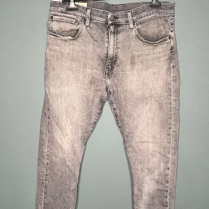 Levi's 512 grå jeans W34 L30 - Grå jeans från Levi's modell 512 med klassisk femficksdesign och smal passform. Jeansen har en snygg tvättad look och är tillverkade i mjukt denimtyg. Perfekta för dig som gillar en modern och stilren vibe.
