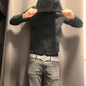 Svart vindjacka med huva - Svart vindjacka med dragkedja och huva. Jackan har en clean look med två sidofickor med dragkedja och en smal passform. Perfekt för dig som gillar stilren streetwear. från nike