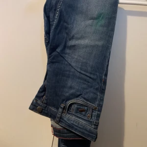 Blå jeans med dragkedja vid benslut - Säljer ett par blå jeans med snygga detaljer som dragkedja och knapp vid benslutet. Jeansen har klassisk femficksdesign och en cool tvättad look. Perfekta för dig som gillar en avslappnad stil med lite edge. Har grön fläck