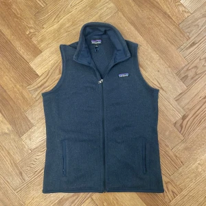 Patagonia väst blå  - Mysig mörkblå fleeceväst från Patagonia med hög krage och hel dragkedja framtill. Västen har två fickor med dragkedja och klassisk logga på bröstet. Perfekt för hösten vintern och skidbacken!