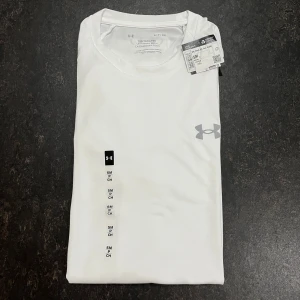 Under armour t shirt Stl S - Snygg vit t-shirt från Under Armour med klassisk rund hals och diskret logga på bröstet. Tillverkad i ett lätt och funktionellt syntetmaterial som andas, perfekt för träning eller en aktiv vardag. Modellen har korta ärmar och en loose passform.