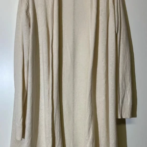 Beige långärmad kofta KappAhl - En stilren och enkel beige långkofta från KappAhl i mjukt material. Koftan har lång ärm och rak passform, perfekt för dig som gillar en clean och avslappnad look. Passar till många olika tillfällen och är superenkel att styla.