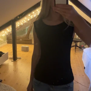 Svart ärmlös topp från Vero Moda XS - Enkel och stilren svart topp från Vero Moda i storlek XS. Toppen är ärmlös med rund halsringning och rak passform. Perfekt att matcha med jeans eller kjol för en clean look. Tillverkad i mjuk bomull för skön känsla hela dagen.