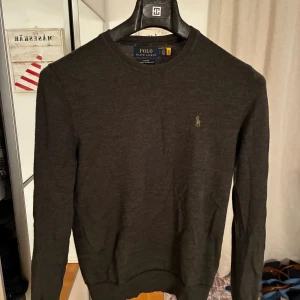 Polo Ralph Lauren tröja i merinoull  - Snygg olivgrön stickad tröja från Polo Ralph Lauren i tvättbar merinoull. Slim fit-modell med rund halsringning och diskret broderad logga på bröstet. Perfekt för dig som gillar klassisk och stilren look. Nypris cirka 1700kr