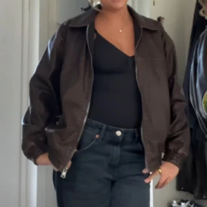 Brun skinnjacka med dragkedja - Säljer en brun skinnjacka i klassisk bombermodell med dragkedja framtill och resår vid ärmslut och nederkant. Jackan är lite oversize men slutar precis vid rumpan. 