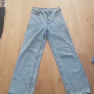 Ljusblå raka jeans med hög midja - Säljer ett par ljusblå jeans med klassisk femficksdesign och raka ben. Jeansen har hög midja och är tillverkade i jeansmaterial med en snygg, enkel look. Perfekta för dig som gillar en avslappnad och trendig stil. PRIS KAN DISKUTERAS!