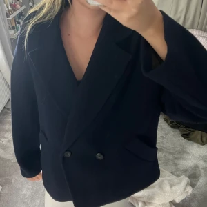 Mörkblå kappa  - Snygg mörkblå kappa med klassisk dubbelknäppning och breda slag. Jackan har två fickor framtill och en rak, något oversized passform. Perfekt för dig som gillar stilrena och tidlösa plagg.