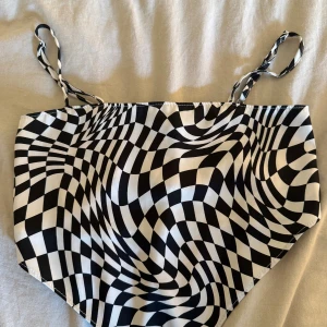 Svartvit mönstrad linnetopp H&M Divided - Säljer en svartvit linnetopp från H&M Divided med ett coolt optiskt rutmönster. Toppen har smala axelband och smockad rygg för extra komfort. Materialet är mjukt och lätt, perfekt för att sticka ut med en unik look.