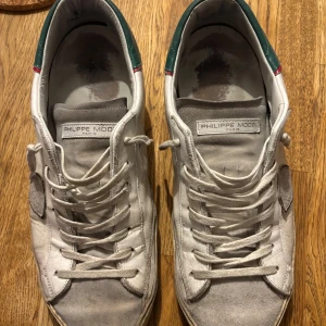Philippe Model vita sneakers med gröna detaljer - Snygga vita sneakers från Philippe Model med gröna och röda detaljer vid hälen. Lite slitna därav priset men dom är fortfarande fullt fungerande och ser bra ut på fötterna😊 Storlek 43.