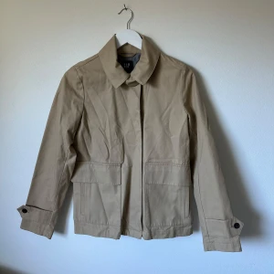 Beige rock från GAP med fickor - Snygg beige rock från GAP i storlek S (jag har skrivit att den är i XS i beskrivningen för att den är lite liten i storleken). Jackan har klassisk krage, stora fickor framtill och knappar vid ärmslut. Tillverkad i bomullsmaterial och har en stilren, rak passform. Perfekt för dig som gillar minimalistisk och clean stil. 3Z7