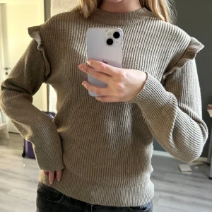 Brun stickad tröja med volang - Brun stickad tröja med ribbad struktur och volangdetaljer på axlarna.