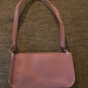Ljusrosa axelväska med krokoprägling - Säljer en ljusrosa axelväska med trendig krokopräglad yta. Väskan har en stilren, rektangulär form och bred axelrem. Perfekt accessoar för att lyfta din outfit med en poppig färg och cool struktur.