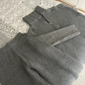 Grå ribbstickade mjukisbyxor - Mysiga grå ribbstickade mjukisbyxor med bred mudd i midjan och vid benslut. Byxorna har dragkedja vid benslutet för extra stil och funktion. Perfekta för chill dagar hemma eller när du vill vara bekväm men ändå se snygg ut.