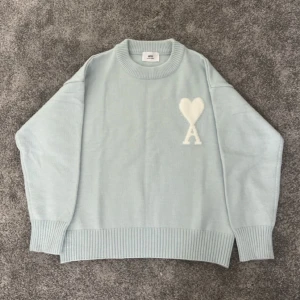 Ljusblå stickad tröja från Ami Paris storlek S - Superfin ljusblå stickad tröja från Ami Paris med ikoniskt hjärta och A-logga i vitt på bröstet. Och är bara använd 2 gånger.Tröjan har rund hals, breda ribbade muddar och en loose fit som ger en chill vibe. Perfekt för lager-på-lager under kyliga dagar.                       