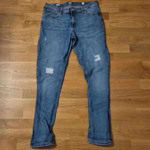 Blå skinny jeans från Jack & Jones - Snygga blå jeans från Jack & Jones med skinny passform och klassisk femficksdesign. Jeansen har slitna detaljer på benen, dragkedja i gylfen och ljus tvätt. Perfekta för dig som gillar en smal siluett och modern look.