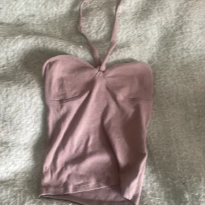 Ljuslila halterneck topp Gina Tricot XS - Supersöt ljuslila halterneck topp från Gina Tricot i ribbat material. Toppen har en bandeau-liknande form med knyt runt nacken och markerade kupor. Perfekt för dig som gillar en enkel men trendig look.